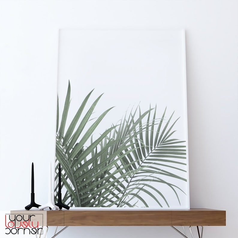 May include: A white framed print of a green palm leaf on a white background. The print is sitting on a wooden shelf with two black candle holders.