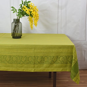Könnte beinhalten: Eine limettengrüne Tischdecke mit dekorativem Blumenmuster. Eine Vase mit gelben Blumen und grünen Blättern steht auf dem Tisch. Die Tischdecke ist über einen dunkelbraunen Tisch drapiert.