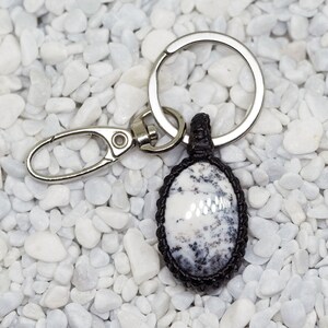 May include: A white and black agate stone keychain with a black cord and silver metal ring.
