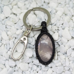 May include: A black and silver keychain with a small oval-shaped charm. The charm has a black border and a cloudy, light grey image inside.