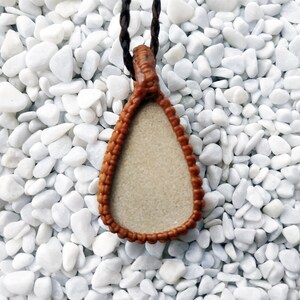 May include: A brown leather pendant with a teardrop shape and a white center. The pendant is hanging from a brown cord.
