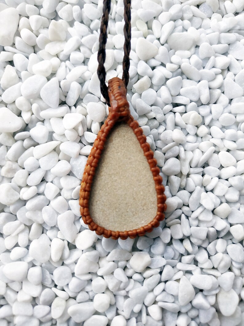 May include: A brown leather pendant with a teardrop shape and a white center. The pendant is hanging from a brown cord.