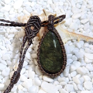 May include: A dark green gemstone pendant with a brown macrame cord necklace. The pendant is teardrop shaped and has a natural, organic look.