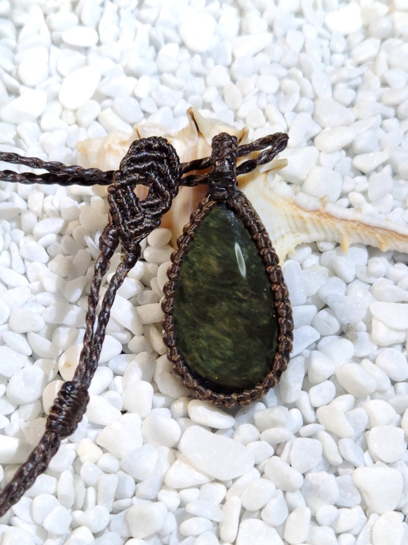 May include: A dark green gemstone pendant with a brown macrame cord necklace. The pendant is teardrop shaped and has a natural, organic look.