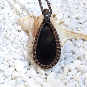 May include: A black gemstone pendant with a brown leather cord. The pendant is in the shape of a teardrop and is surrounded by a brown braided cord.