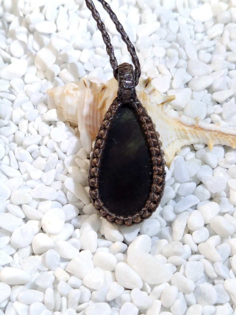 May include: A black gemstone pendant with a brown leather cord. The pendant is in the shape of a teardrop and is surrounded by a brown braided cord.