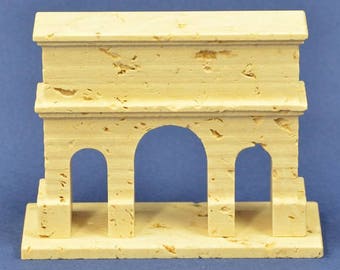 May include: A small, cream-colored model of an archway with three openings. The model is made of a textured material that resembles stone.