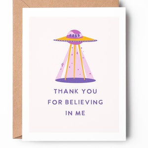 May include: A pink and yellow UFO with a light pink background. The text reads "Thank you for believing in me."
