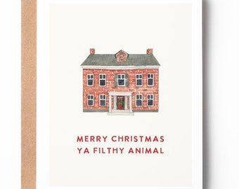 May include: A Christmas card featuring a red brick house with a white door and a green roof. The text "Merry Christmas Ya Filthy Animal" is printed below the house.
