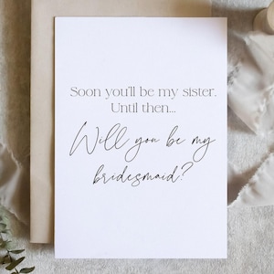 May include: A white card with black text that reads "Soon you'll be my sister. Until then... Will you be my bridesmaid?"
