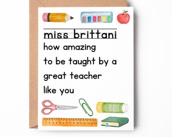 May include: A white card with a brown envelope behind it. The card has a black and white message that reads "miss brittani how amazing to be taught by a great teacher like you". The card is decorated with watercolor illustrations of school supplies, including a pencil, paint palette, apple, scissors, paper clips, glue stick, ruler, and a book.