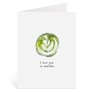 May include: A white greeting card with a watercolor illustration of a green matcha latte design. The card reads "I love you so matcha" in black text.
