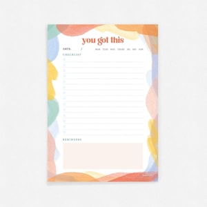Peut inclure: Un bloc-notes de liste de contrôle coloré avec le texte "you got this" en gras, en orange. Le bloc-notes comporte une section de liste de contrôle, une section de rappels et une section de date. L'arrière-plan est un design aquarelle avec des formes abstraites dans des tons de bleu, jaune, orange et rose.