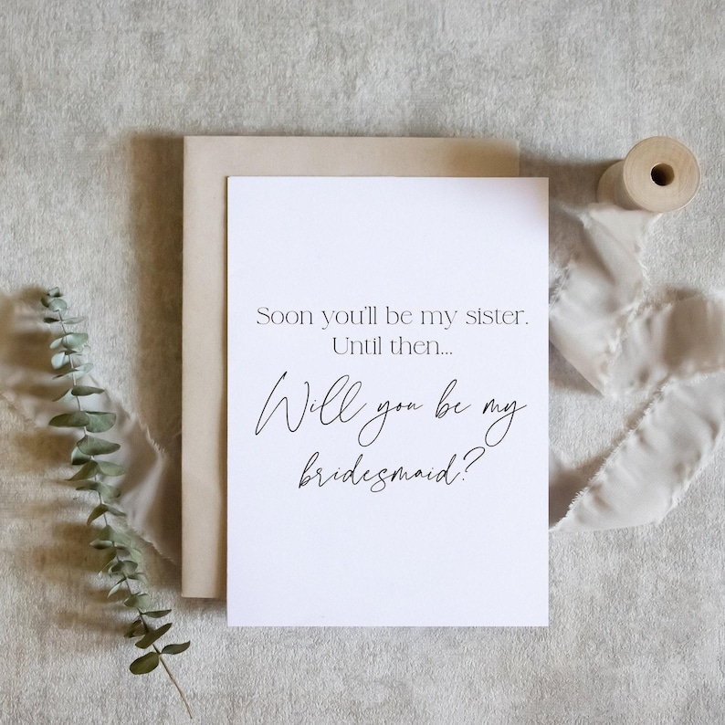 May include: A white card with black text that reads "Soon you'll be my sister. Until then... Will you be my bridesmaid?"