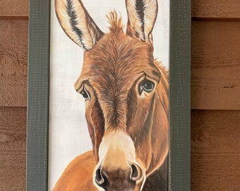 May include: A framed painting of a brown donkey with large ears. The donkey is looking directly at the viewer with a curious expression. The painting is set against a white background.