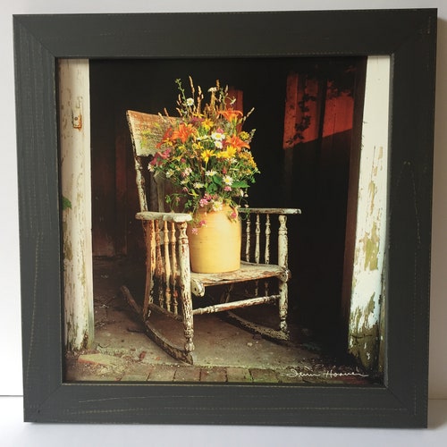 Old rocking chair with paint peeling with beautiful flowers in a crock that is on the chair Farmhouse style framed picture Primitive
