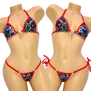 May include: A two-piece bikini set with a vibrant leopard print in shades of blue, purple, yellow, and green. The bikini features red trim and ties, with rhinestone accents on the top. The triangle top and string bottom create a stylish look.