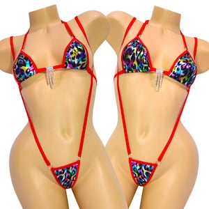 May include: A two-piece bikini set with a vibrant leopard print in shades of blue, purple, yellow, and green. The bikini features red straps and trim, with a rhinestone accent on the top. The bottoms are a thong style.