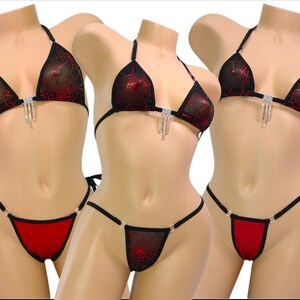 May include: A black and red bikini set with a halter top and string tie bottoms. The top features a sheer overlay with a red spiderweb design and a rhinestone embellishment. The bottoms are red with black trim.