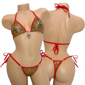 May include: A two-piece bikini set featuring a leopard print pattern with red trim. The top has a jewel accent and ties at the neck and back. The bottom is a thong style with side ties. The bikini is displayed on a mannequin.