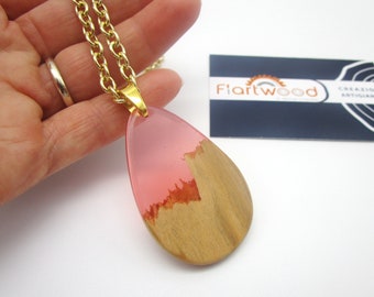 May include: A pink and wood resin pendant necklace with a gold chain. The pendant is shaped like a teardrop and has a wood grain pattern on the bottom half. The top half is a translucent pink resin.