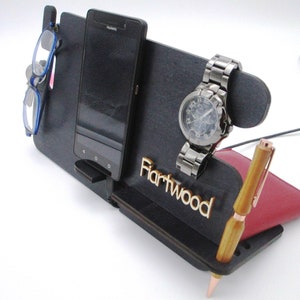 Może przedstawiać: Czarny drewniany organizer na biurko z miejscami na telefon, zegarek, długopis i okulary. Organizer ma wygrawerowane słowo "Hartwood" na przodzie.