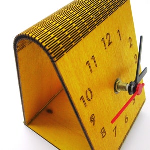 May include: A wooden clock with a yellow finish and black numbers. The clock has a red second hand and black hour and minute hands. The clock is on a white background.