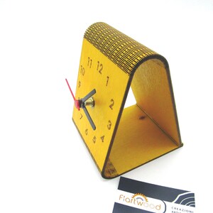 May include: A yellow wooden clock with black numbers and a red second hand. The clock is standing on a yellow wooden stand.