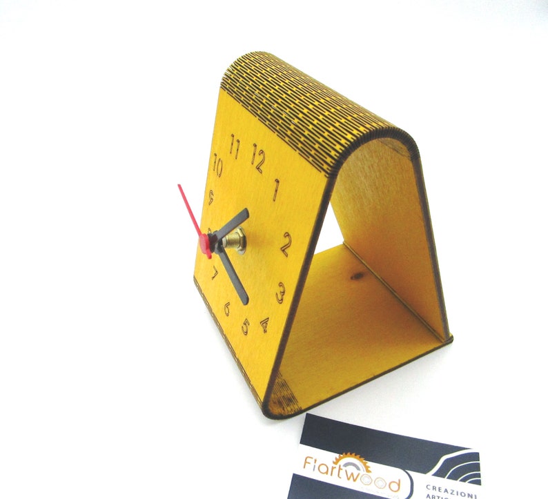 May include: A yellow wooden clock with black numbers and a red second hand. The clock is standing on a yellow wooden stand.
