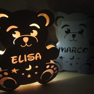 May include: Two wooden bear night lights with cut-out designs. The bear on the left is black and has the name "ELISA" on its belly. The bear on the right is white and has the name "MARCO" on its belly.