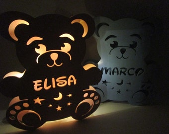 May include: Two wooden bear night lights with cut-out designs. The bear on the left is black and has the name "ELISA" on its belly. The bear on the right is white and has the name "MARCO" on its belly.