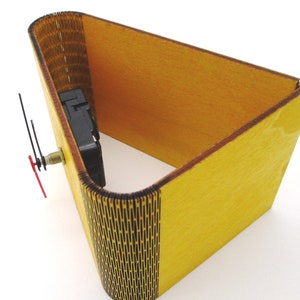 May include: A yellow wooden clock kit with a black clock mechanism and hands. The clock is in the shape of a cube with one side open.