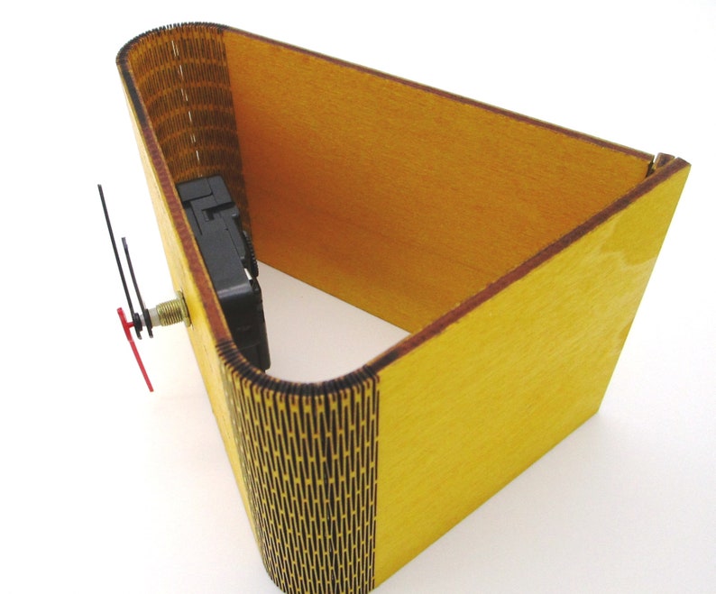 May include: A yellow wooden clock kit with a black clock mechanism and hands. The clock is in the shape of a cube with one side open.