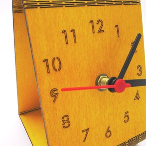 May include: A wooden clock with black and red hands. The clock face is yellow and has black numbers 1 through 12.