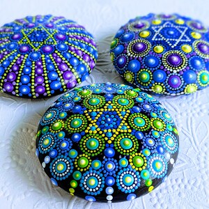 May include: Three painted rocks with a blue, green, and purple mandala design. Each rock features a star of David in the center.