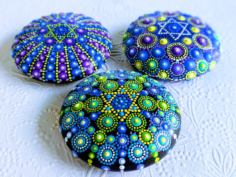 May include: Three painted rocks with a blue, green, and purple mandala design. Each rock features a star of David in the center.