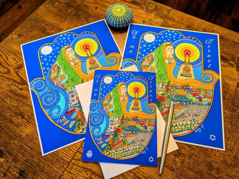 May include: Two blue and yellow Hamsa hand cards with the word "Israel" and "Shema" on them. The cards are decorated with colorful illustrations of Jerusalem and the Western Wall.