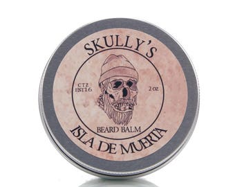 May include: A silver tin with a label that says "Skully's Beard Balm Isla De Muerta" with a skull wearing a beanie hat and a beard. The label is pink and white with black text. The tin is 2 oz.