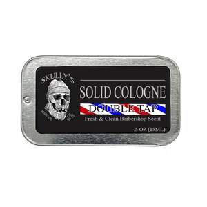 Op de afbeelding: Een zilveren blik met een zwart label waarop staat "SKULLY'S SOLID COLOGNE DOUBLE TAP Fresh & Clean Barbershop Scent .5 OZ (15ML)". Het label toont een schedel met een baard en een muts, en een rood-wit-blauwe barbierstreep.