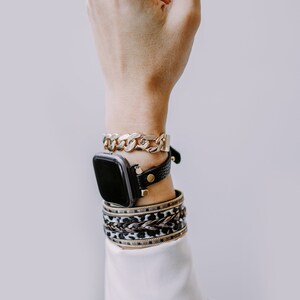 Peut inclure: Un poignet de femme avec un bracelet de montre en cuir noir et un bracelet en cha&icirc;ne dor&eacute;e. Le cadran de la montre est noir et carr&eacute;. La femme porte plusieurs bracelets au poignet, dont un bracelet &agrave; imprim&eacute; l&eacute;opard et un bracelet en or.
