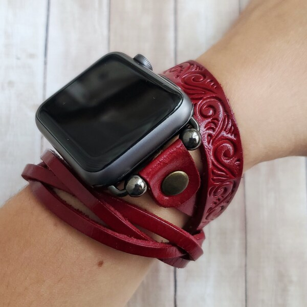 Puede incluir: Una pulsera de reloj de cuero rojo con un diseño decorativo. La pulsera está envuelta alrededor de una muñeca y tiene un Apple Watch plateado adjunto.