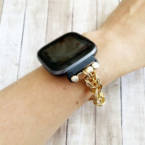 May include: A black smartwatch with a gold chain band. The watch face is black and the band is made of a series of gold chain links.
