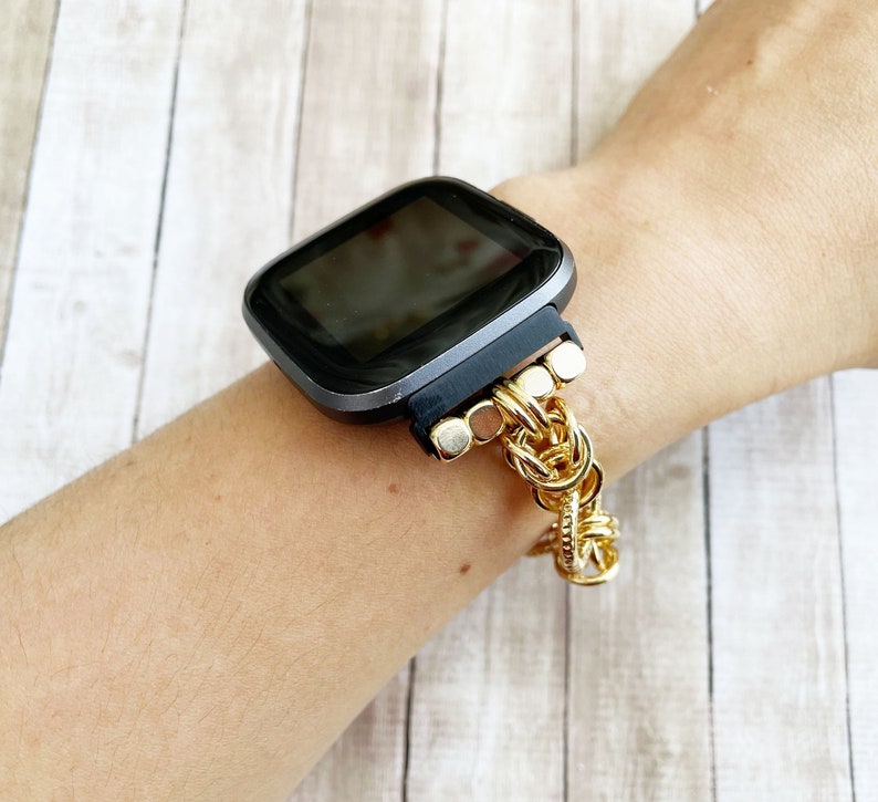 May include: A black smartwatch with a gold chain band. The watch face is black and the band is made of a series of gold chain links.