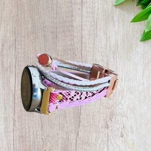 K&ouml;nnte beinhalten: Ein mehrstr&auml;ngiges Uhrenarmband in Rosa-, Wei&szlig;- und Silbert&ouml;nen mit einem ros&eacute;goldenen Verschluss. Das Armband hat geflochtene und gemusterte Elemente und ist an einer silbernen Smartwatch befestigt.