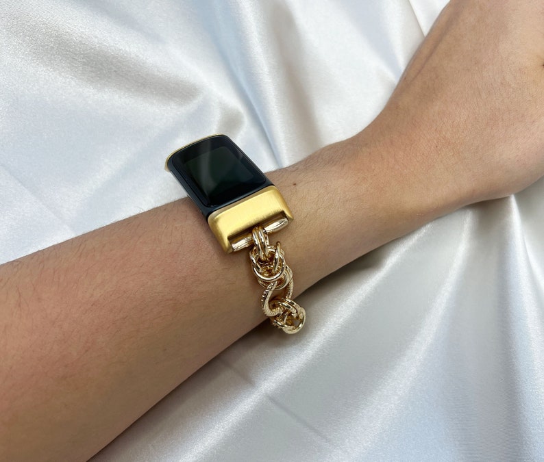 May include: A black and gold fitness tracker with a chain link band.
