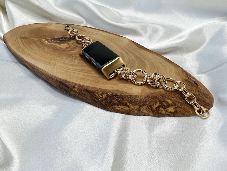 May include: A gold chain bracelet with a black rectangular watch face. The bracelet is on a wooden surface.