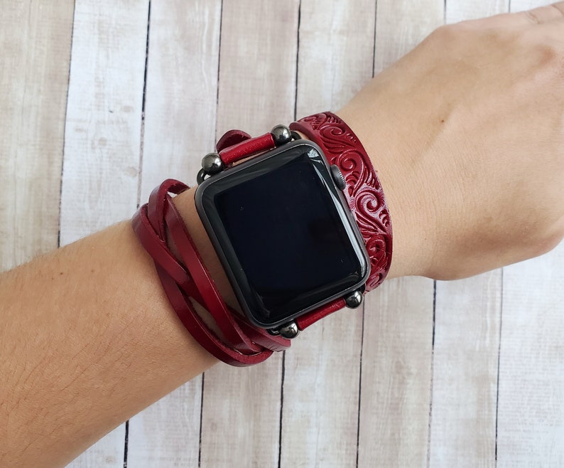 Może przedstawiać: Czerwony sk&oacute;rzany pasek do zegarka Apple z plecionym wzorem i tłoczonym wzorem kwiatowym. Pasek jest noszony na nadgarstku.