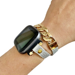 Peut inclure: Une montre connect&eacute;e avec un cadran noir et un bracelet en cuir blanc avec un bracelet &agrave; maillons dor&eacute;s par-dessus.