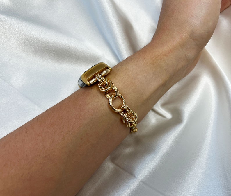 May include: A gold chain watch band with a silver watch face. The band is made of thick, linked chains.