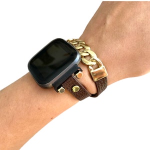 Peut inclure: Un bracelet de montre en cuir marron avec un bracelet en cha&icirc;ne dor&eacute;e sur le dessus. Le bracelet de montre a des accents dor&eacute;s et est port&eacute; au poignet.